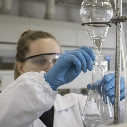 Profissional de laboratório usando luvas e vidraria para análise química, simbolizando assessoria técnica química e controle de processos. Profissional de laboratório usando luvas e vidraria para análise química, simbolizando assessoria técnica química e controle de processos.