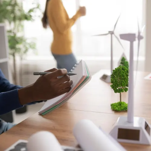 Analista anotando dados ao lado de maquete de turbina eólica, simbolizando estudos ambientais para empreendimentos. Analista anotando dados ao lado de maquete de turbina eólica, simbolizando estudos ambientais para empreendimentos.